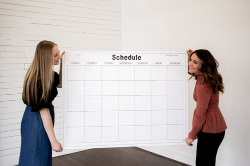 large wall calendar activities and schedule held by two women